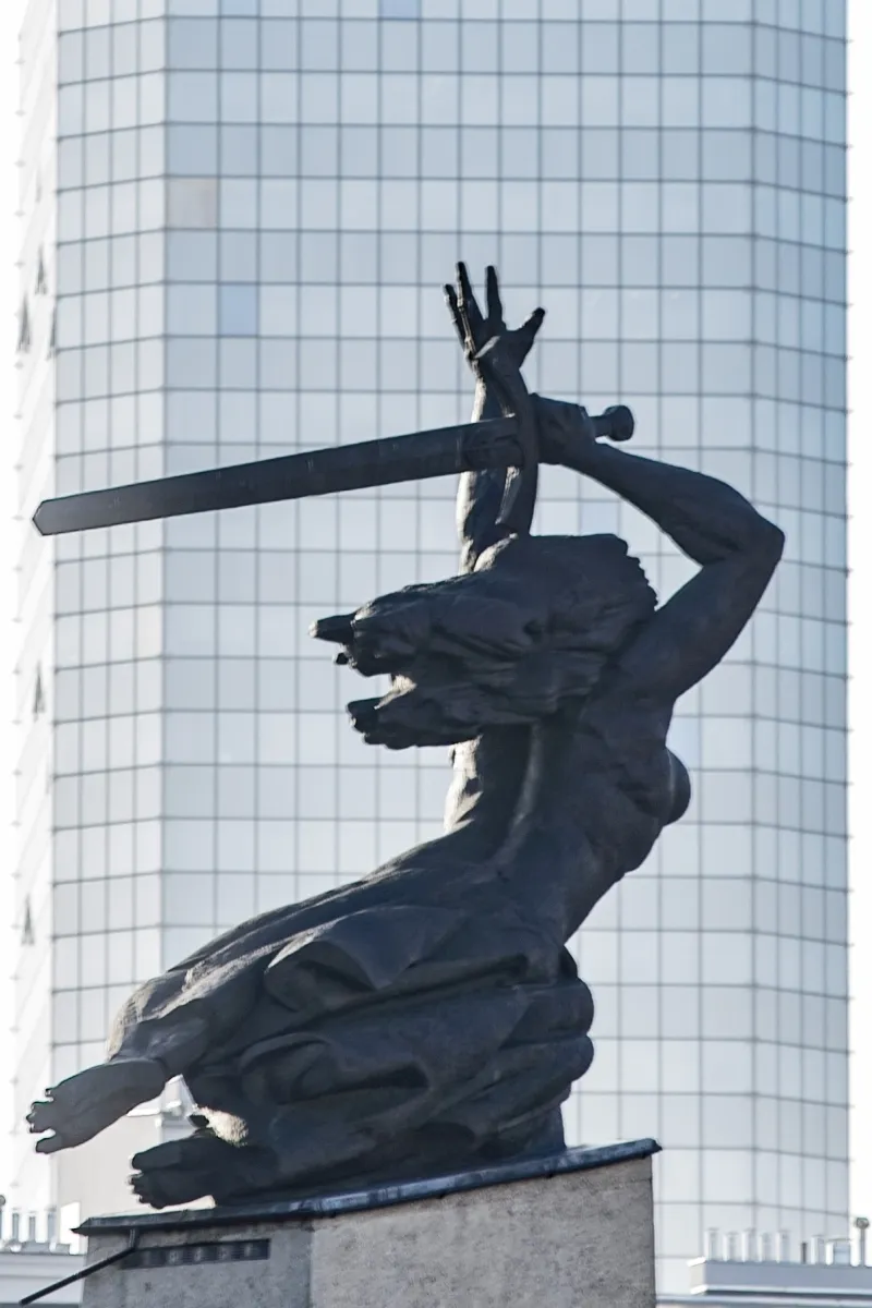 Dark statue raising a sword before a glass skyscraper